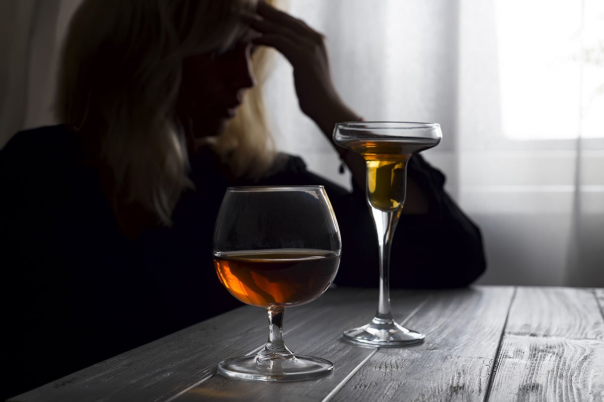 woman in darkness with two drinks experiencing the dangers of binge drinking