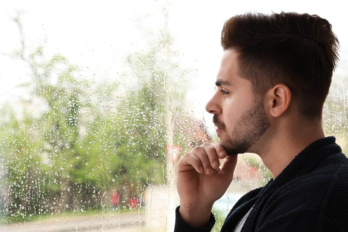 man looking out window thinking about cycle of addiction