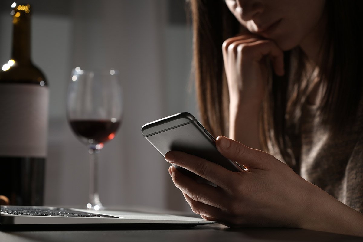 woman with glass of wine and searching on her device drinking and social media