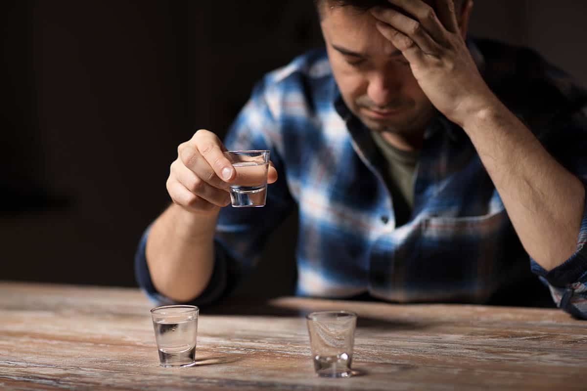 a man taking shots thinking about how he should be getting help for an alcoholic man